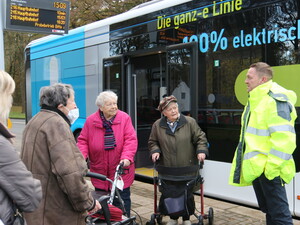 Bild vom Rollatortraining an einer Bushaltestelle. Mehrere ältere Personen stehen vor dem Bus.