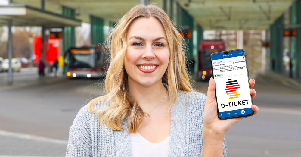 Frau am Bahnhof hält ihr Handy hoch. Zu sehen ist das Deutschlandticket